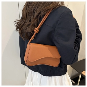 Brown leather crossbody bag featuring a curved flap and decorative knot strap detail