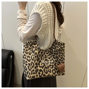 Detail of leopard print canvas tote bag featuring brown leather straps and small pendant
