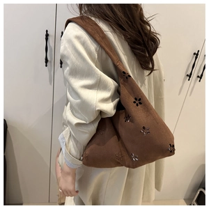 Detail of a brown faux suede shoulder bag with laser-cut floral patterns on a model