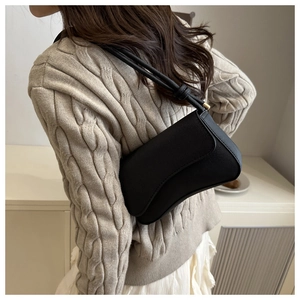 Detailed view of a black crescent shoulder bag with knotted strap on a textured sweater