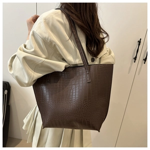 Detailed texture of brown crocodile-embossed tote bag worn over a beige coat