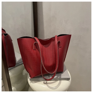 Detail of red crocodile texture tote bag with slim handles on a white artistic stool