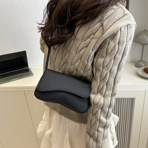 Minimalist black crossbody bag with a wave-shaped flap design on a textured leather surface