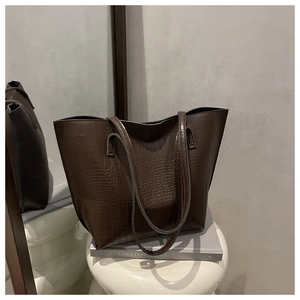 Detail of dark brown tote bag with crocodile texture placed on a minimalist stool