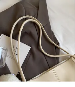 Detail of cream-colored tote bag featuring slender shoulder straps and silver ball chain accent