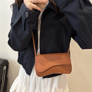 Chic brown crossbody bag with unique wavy flap design worn by model over a jacket