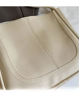 Detail showing smooth beige leather texture and fine stitching on a minimalist bucket bag
