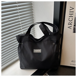 Detail view of the black tote bag featuring a Fashion label and side drawstring adjustment