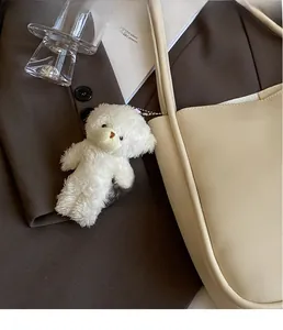 Cute white plush bear charm with metal chain detail on a beige leather tote bag