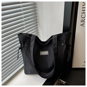 Detailed close-up of a black nylon tote bag with side drawstrings and a Fashion logo patch