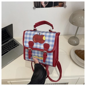 Blue and white plaid mini backpack with red apple prints on a desk in lifestyle setting