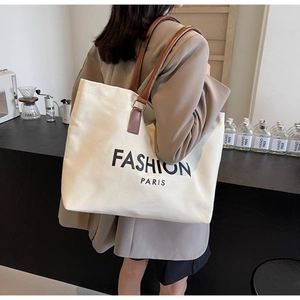 Primer plano de un bolso tote de lona crema con asas de cuero marrón y estampado chic
