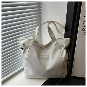 Detail of white canvas tote bag featuring fashion label and side drawstring adjustment