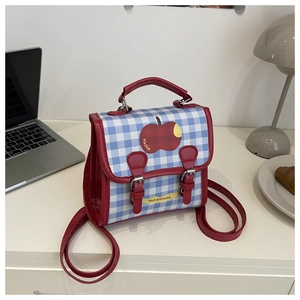 Detail of red and blue plaid backpack featuring apple print on a cozy desktop scene