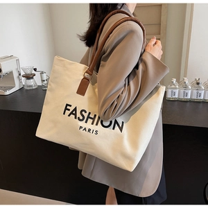 Primer plano del bolso tote de lona beige con asas de cuero marrón y texto impreso