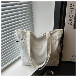 Detailed shot of white tote bag featuring fashion patch and drawstring side adjustments