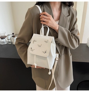 Close-up of white leather backpack with silver butterfly accents and drawstring detail