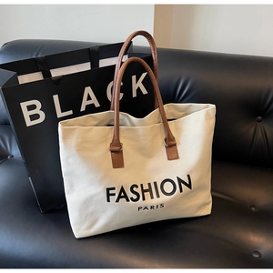 Detalle de bolso tote de lona beige con asas de cuero marrón sobre un sofá de cuero negro