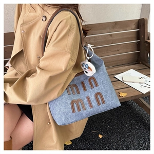 Detail of light blue denim tote bag with brown leather handles and plush doll pendant