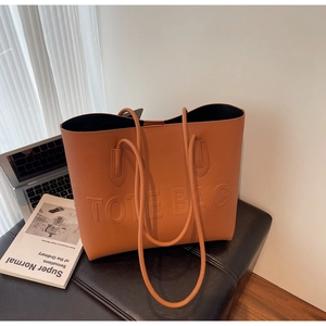 Détail d'un cabas marron caramel avec texte TOTE BAG embossé sur un tabouret en cuir noir