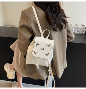 Rear view of model wearing a white mini backpack with silver butterfly accents