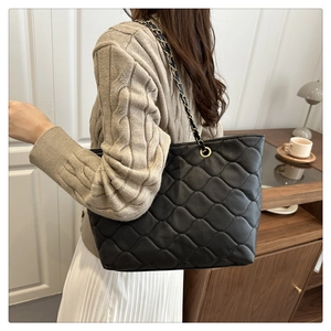 Close-up of a black quilted tote bag with golden chain strap in a lifestyle setting