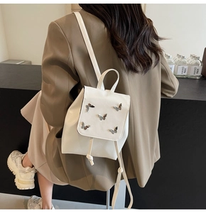 Chic white mini backpack with silver butterfly accents shown on a model in beige suit
