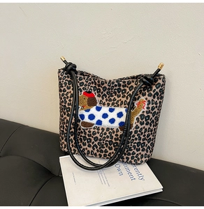 Détail du sac cabas léopard avec broderie teckel posé sur un canapé en cuir noir