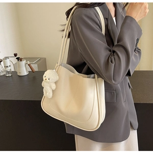 Minimalist cream white tote bag with bear charm shown in a cozy city commute setting