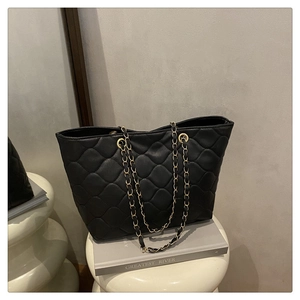 Detail of black quilted tote bag featuring large diamond stitching and woven gold chain straps
