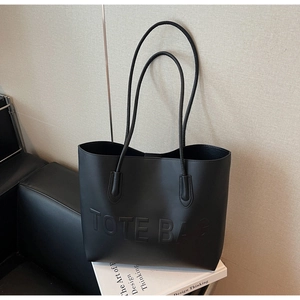 Détail d'un sac cabas en cuir noir mat avec lettres embossées et fines bandoulières doubles