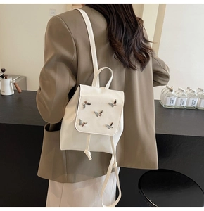Detail of white leather mini backpack featuring decorative metal butterflies and drawstring