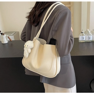Detail of a creamy white tote bag with vertical stitching and a cute bear charm