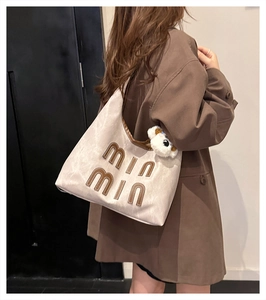 Detail of a beige tote bag with brown trim, min min lettering and a cute bear plush pendant