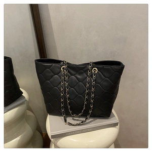 Détail d'un sac cabas noir matelassé avec chaîne dorée posé sur un support artistique