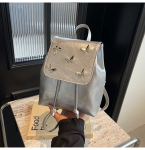 Detail of silver metallic mini backpack featuring 3D metal butterfly ornaments on the flap