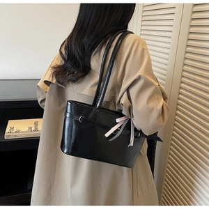 Dettaglio borsa tote in pelle verniciata nera con elegante ciondolo a fiocco rosa