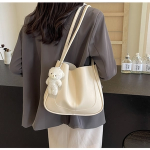 Detail of cream leather shoulder bag with decorative stitching and cute teddy bear charm