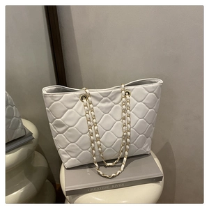 Detail shot of white quilted tote bag with gold woven chain straps and elegant texture