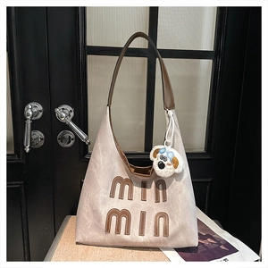 Detail of grey tote bag with brown leather handles and a plush puppy charm on a door