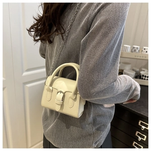 Close-up of a cream leather mini bag with silver chain strap worn with a grey knit sweater