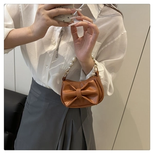Mirror selfie showing a brown mini handbag with oversized bow and pearl handle details