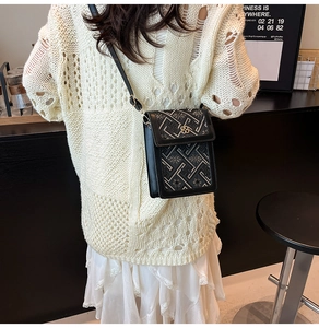 Chic black crossbody bag with floral gold clasp and embroidery texture worn over white knit