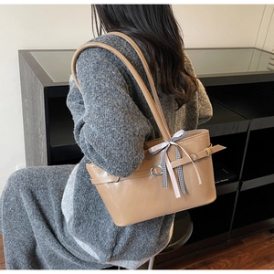Dettaglio della borsa sottobraccio color cammello con fiocco a quadretti e finitura lucida