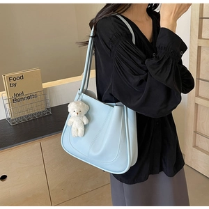 Detail shot of light blue tote bag with plush bear charm and thin shoulder strap