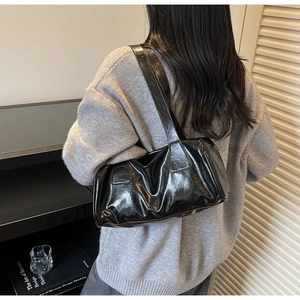 Detalle del bolso de hombro en charol negro con textura plisada y piezas metálicas