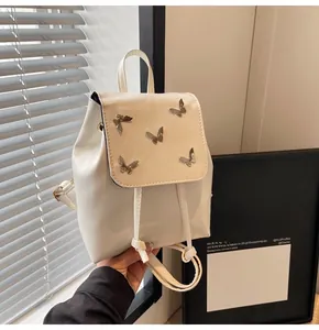 Detail of cream white mini backpack featuring metal butterfly charms and drawstring closure