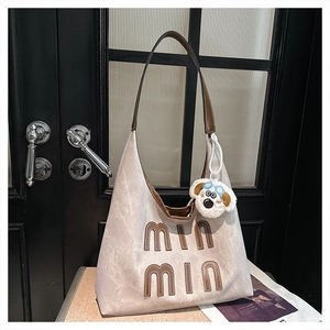 Close-up of beige canvas tote with brown leather trim and plush puppy charm detail