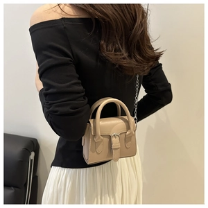 Detail of a beige mini bag with a metal buckle and silver chain strap on a model