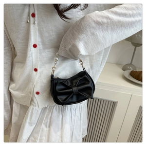 Detail of black bow shoulder bag with pearl handle worn by a model in a chic setting